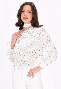 Weißes Blusenshirt mit schwarzen Punkten, rüschigem Kragen und Manschetten, langen Ärmeln und einem hohen, festen Halsbündchen. Leichtes, durchsichtiges Material.