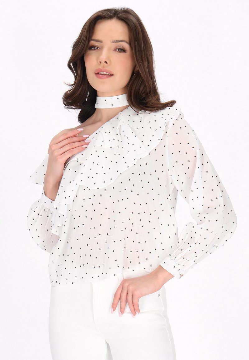 Weißes Blusenshirt mit schwarzen Punkten, rüschigem Kragen und Manschetten, langen Ärmeln und einem hohen, festen Halsbündchen. Leichtes, durchsichtiges Material.