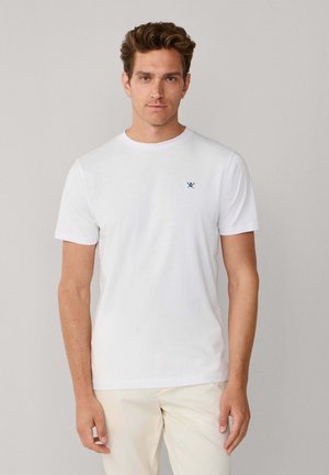 T-shirt en coton blanc à manches courtes, col rond, avec un petit logo bleu marine sur la poitrine gauche. Texture lisse, coupe classique, design minimaliste.