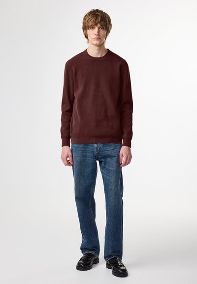Bordeauxfarbener gestrickter Pullover mit Rundhalsausschnitt, kombiniert mit blauen Jeans. Die Passform ist lässig, und die Textur scheint weich und gerippt zu sein.