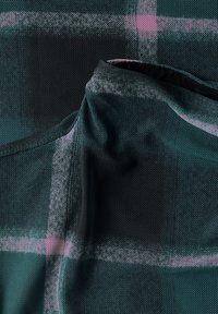 Gros plan sur un tissu en maille vert foncé avec un motif à carreaux violet clair et une partie de col pliée.