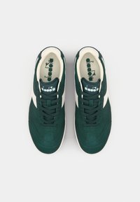 Green suede sneakers with white accents, featuring a rounded toe, lace-up design, and a cushioned insole with logo print.