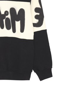 Sweatshirt nero e crema con audace testo in stile graffiti nero. Texture morbida con polsini e orlo a coste, blocchi di colore a contrasto.