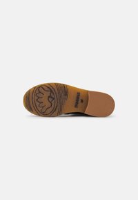 Suola di scarpa in gomma di colore marrone, con un motivo in rilievo e un logo circolare, bordi lisci e una texture leggermente flessibile.