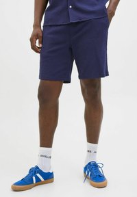 Shorts texturés bleu marine avec une finition soignée, associés à des baskets bleues et des chaussettes blanches avec du texte noir.