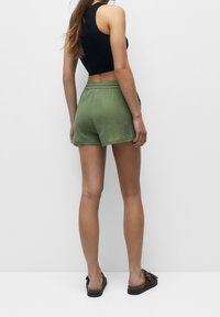 Pantaloni corti verdi in lino con vita elastica, dal taglio rilassato. Abbinati a sandali neri, lo sfondo è bianco semplice.