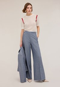 Blusa de punto blanca con detalles rojos, combinada con pantalones anchos azules con botones laterales y una blazer azul. Tacones beige de punta.
