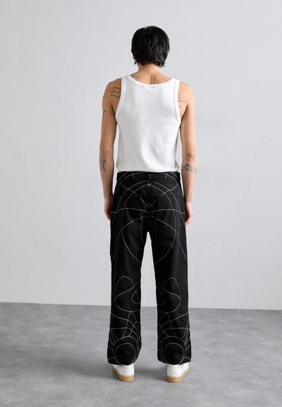 Pantaloni negri cu broderie geometrică albă, asortați cu un top alb fără mâneci. Materialul este moale, cu o croială lejeră și un design cu picioare largi.