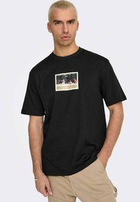 T-shirt in cotone nero con stampa grafica rettangolare di una scena sportiva sulla parte anteriore. Maniche corte e scollatura a girocollo.
