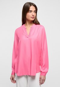 Blusa rosa a maniche lunghe con scollatura a V e un sottile spacco frontale. Tessuto liscio simile alla satinato, vestibilità leggermente ampia, orlo curvo.