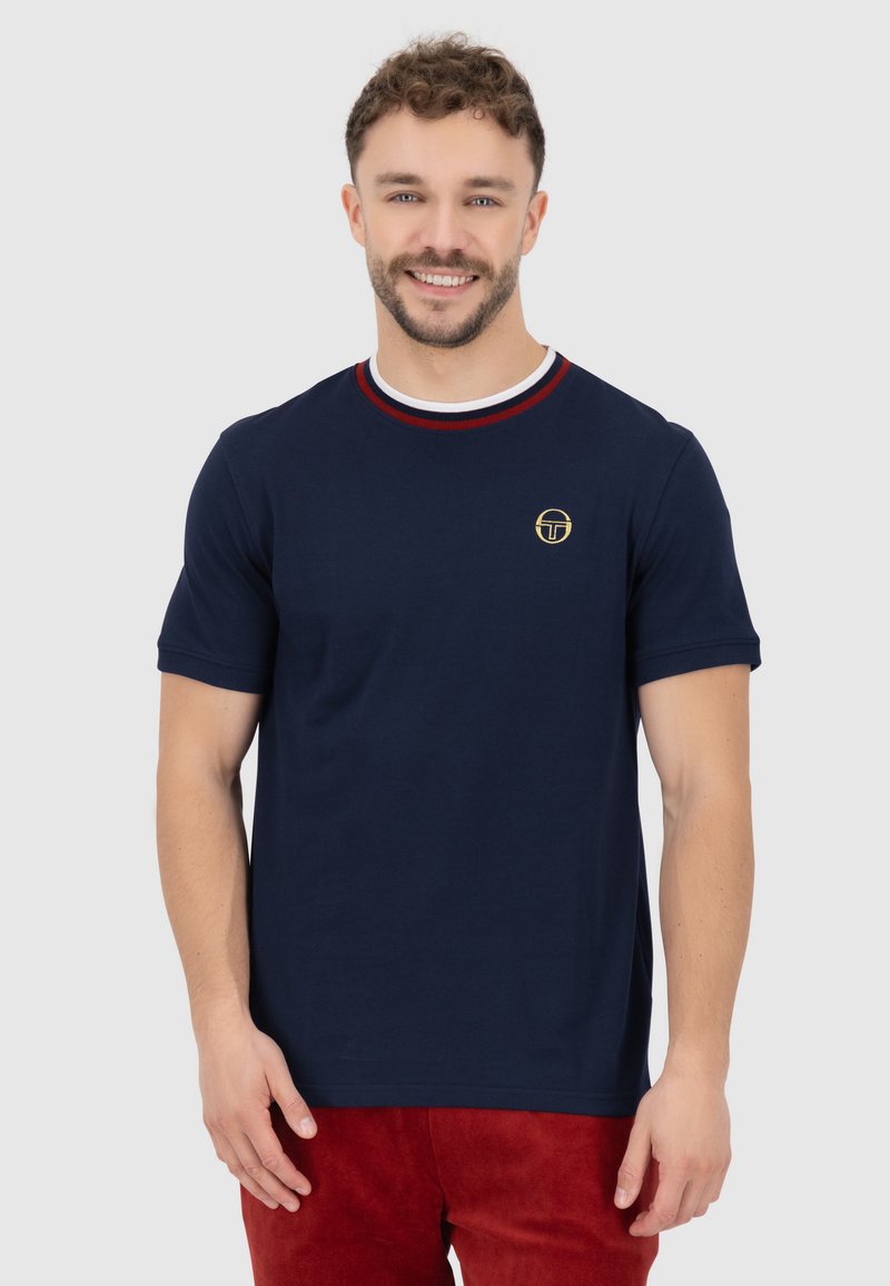 Navyblauwe katoenen t-shirt met ronde hals en rode en witte gestreepte accenten, en een klein goudkleurig logo op de borst. Korte mouwen.