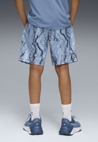 Bermudas azuis com um padrão de grelha e um design ondulado, feitas de tecido leve, combinadas com sapatilhas azuis e meias brancas.