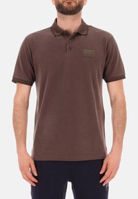 Polo shirt marrone realizzato in cotone, con colletto, tre bottoni e un'etichetta rettangolare sul petto sinistro.