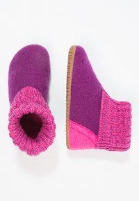 Filcowe kapcie w kolorze fioletowym i różowym, z dzianinowym mankietem i gumową podeszwą, z kontrastującymi kształtami i fakturami na cholewce i podeszwie.