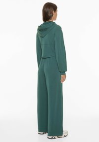 Haut à capuche vert court avec une capuche, pantalon assorti à jambes larges. Tissu doux avec une finition texturée, présentant des manches longues et des poches latérales.