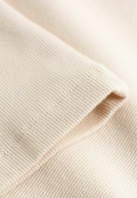 Gros plan sur un tissu beige côtelé avec des coutures détaillées le long d'un bord plié.