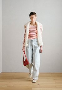 Κόκκινο και λευκό ριγέ πουκάμισο μακρυμάνικο, κρεμ αμάνικο γιλέκο από ψεύτικη γούνα, ανοιχτό μπλε παντελόνι με φλέβες, μπεζ μπαλαρίνες, μικρή κόκκινη τσάντα.