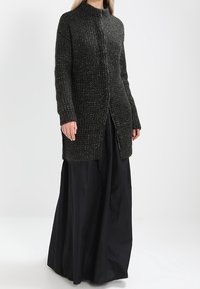 Long black skirt and a dark grey textured cardigan with a high neck, featuring a front button closure and side slits.