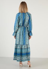Maximekko sinisessä, jossa on monimutkaisia paisley-kuvioita, joustava vyötärö, pitkät hihat, kerättyjä yksityiskohtia ja kerroksellinen helma. Valmistettu kevyestä kankaasta.