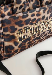 Sac à main à motif léopard avec accents noirs et lettrage doré "VENICE". Fabriqué en tissu texturé, il est doté de deux poignées et d'une bandoulière amovible.