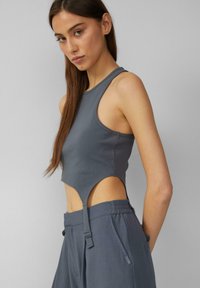 Šedý žebrovaný crop top s výřezy po stranách, s kulatým výstřihem a zakončením s lemem, doplněný o odpovídající šedé kalhoty s vysokým pasem.