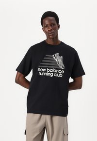 Svart t-skjorte i bomull med en hvit grafikk av en sneaker og teksten "new balance running club" med fet skrift. Avslappet passform og korte ermer.
