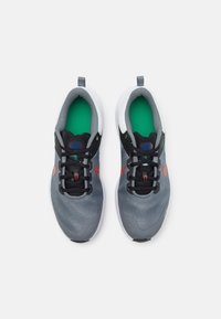 Baskets de sport grises avec des accents noirs et des détails rouges. Présentent une tige en maille texturée, un col rembourré et une semelle intérieure verte. Conçues pour le confort et le soutien.