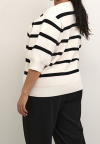 Musta-valkoraidallinen neulepaita, jossa on rento istuvuus, leveät hihat ja joustinneulottu helma, yhdistetty mustiin housuihin. Pehmeä tekstuuri.
