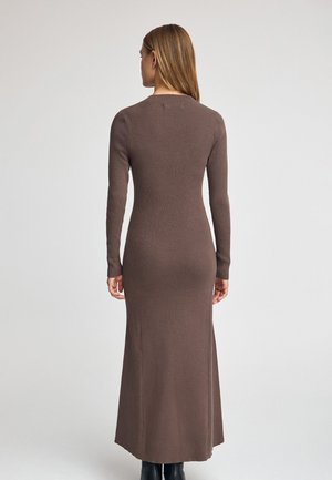 Brown ribbed knit dress with long sleeves, fitted shape, and a maxi length. The back features a rounded neckline and smooth texture.