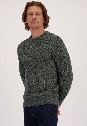 Groene gebreide trui met een textuurpatroon, ronde halslijn en ribbels aan de manchetten. Gecombineerd met donkerblauwe jeans.