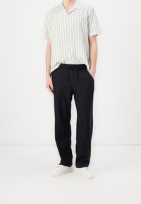 Short-sleeve striped shirt in light green and white, paired with black drawstring pants and white sneakers. Simple, relaxed fit.