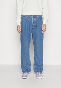 Light-wash denim jeans with a loose fit, featuring belt loops and five-pocket design. Worn with purple checkered slip-on shoes.