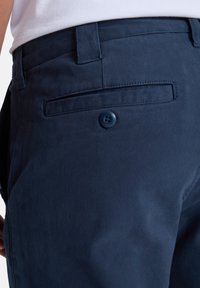 Pantalones de algodón azul marino con un bolsillo trasero que cuenta con un solo botón azul. Textura suave y diseño ajustado.