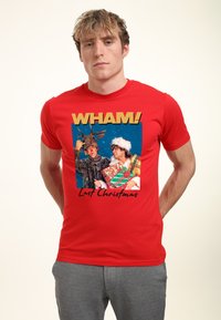 Červené tričko s nápisem "WHAM!" a grafikou dvou lidí v slavnostním oblečení. Design zahrnuje barevné dárkové krabice a sníh.