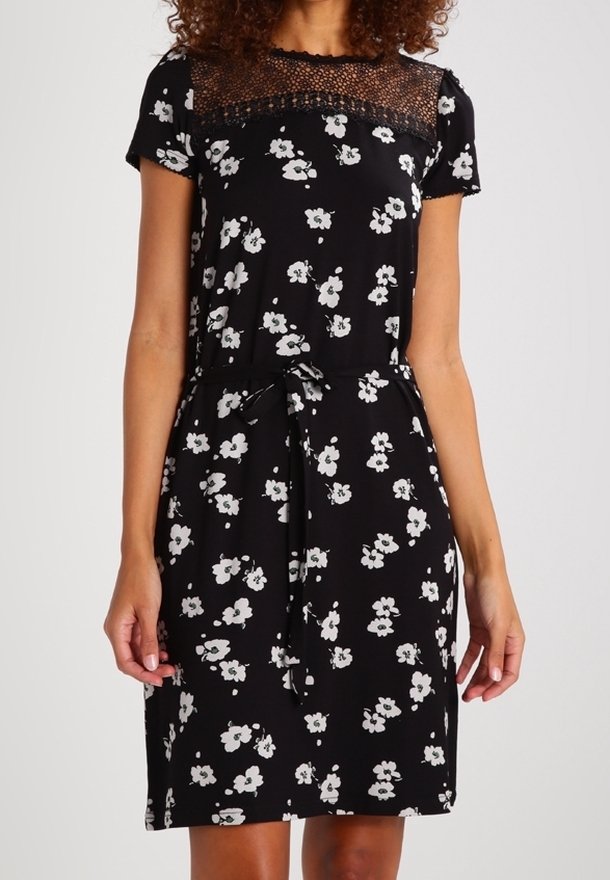 Robe noire longueur genou avec imprimé floral blanc, empiècement en dentelle à l'encolure, manches courtes et ceinture à nouer à la taille.