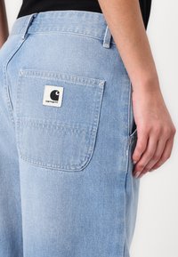 Ljust blå denimbyxor med en bakficka som har en fyrkantig, vit logotyp. Tyget har en mjuk textur och en något urblekt utseende.