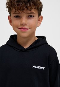 Zwarte hoodie met een voorzak en een trekkoord in de capuchon. Het woord "HUMMEL" is stijlvol in het wit afgedrukt op de linkerborst.