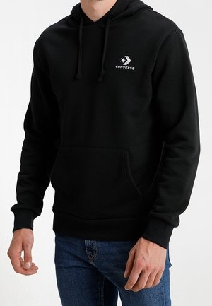 Zwarte Converse-hoodie met zak aan de voorkant en capuchon met trekkoord, gedragen door een persoon in blauwe spijkerbroek tegen een witte achtergrond.