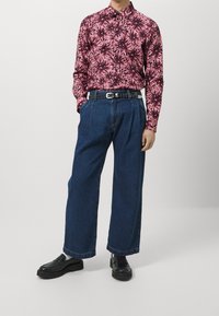 Langärmliges rosa Blumenhemd mit dunkelblauen, hoch taillierten, weiten Denim-Hosen und einem schwarzen Nieten-Gürtel, kombiniert mit schwarzen Slippern.