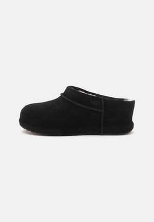 Sort slip-on ruskindstøfler med lav hæl, rundet tå og blødt indre for, synligt ved åbningen, sidevisning.