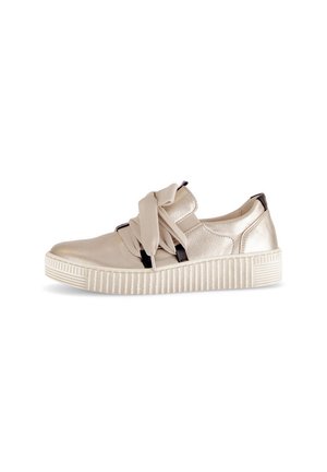 Buty z metaliczną, beżową cholewką ze skóry, zdobione tkaninową kokardą, z czarnymi akcentami oraz teksturowaną, białą gumową podeszwą z pionowymi rowkami.