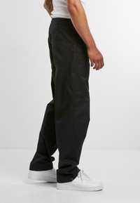 Black cargo pants with a relaxed fit, featuring an elastic waistband and side pockets, paired with white sneakers on a light background.