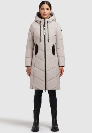 Lichtbeige gewatteerde jas met capuchon, chevronstructuur, ritssluiting, zijzakken en zwarte accenten. Gekocht over zwarte leggings en laarzen.