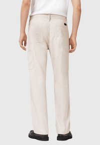 Beige corduroy broek met een losse pasvorm, voorzien van achterzakken en een zwart label. De stof heeft een ribbelstructuur.