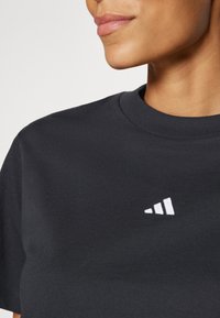 T-shirt noir en coton à col rond avec un petit logo adidas blanc en haut à gauche. Texture lisse et coupe classique.