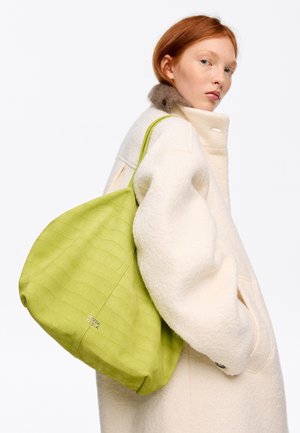 Rohelise tekstuuriga lõuendikott tikandiga mustriga, kandes selle üle õla inimene, kes kannab kreemjat mantel. Vastupidav materjal, suur kuju.