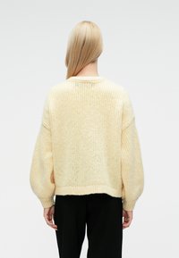 Tekstūruotas, minkštas geltonos spalvos megztinis su didelėmis rankovėmis ir trumpu siluetu. Turi apvalų kaklo iškirpimą bei raštuotą apačią ir rankovių galus.