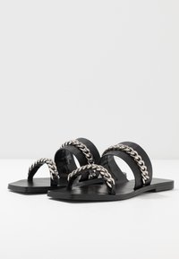 Svarta sandaler har en platt sula och breda remmar med en silverkedjeaccent. Materialet är slätt, med en minimalistisk design och utan utsmyckningar.