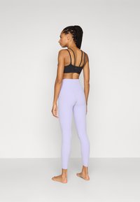 Fekete sportbra, több pánttal, és világos levendula színű, magas derekú leggings. Simás textúra, testre simuló kivitel, és nem látható logók.