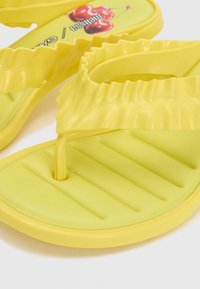 Sandales tongs rembourrées jaunes avec lanières froncées et motif cerise sur la semelle intérieure.